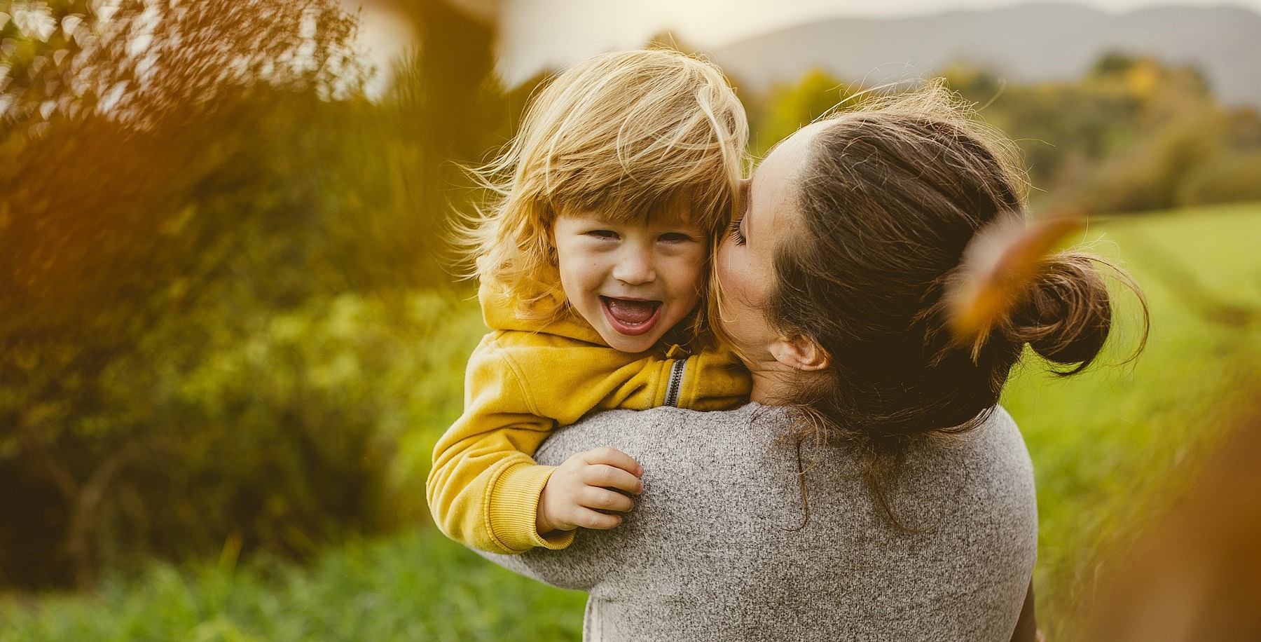 Eine junge Frau steht mit dem Rücken zu Kamera und hat ihre Tochter im Arm.