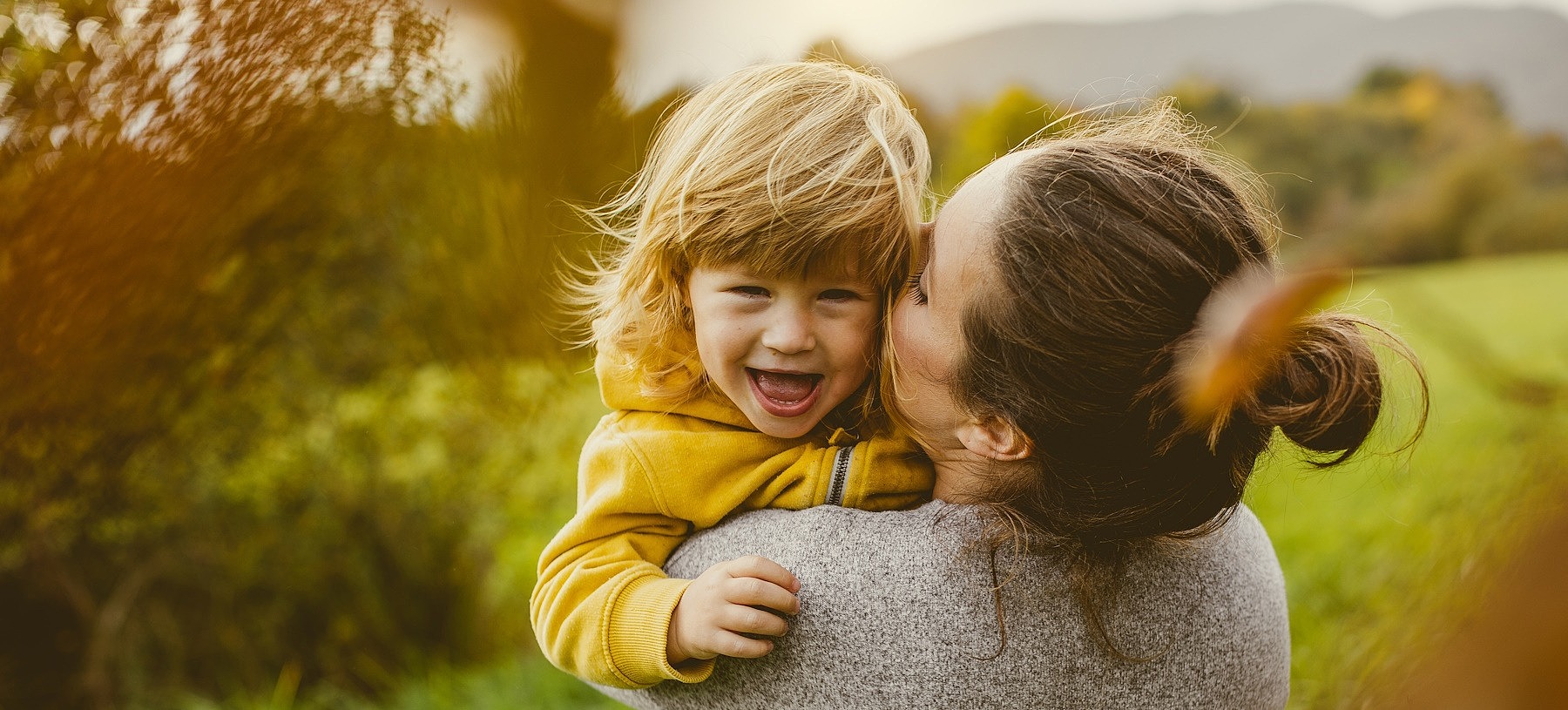 Eine junge Frau steht mit dem Rücken zu Kamera und hat ihre Tochter im Arm.