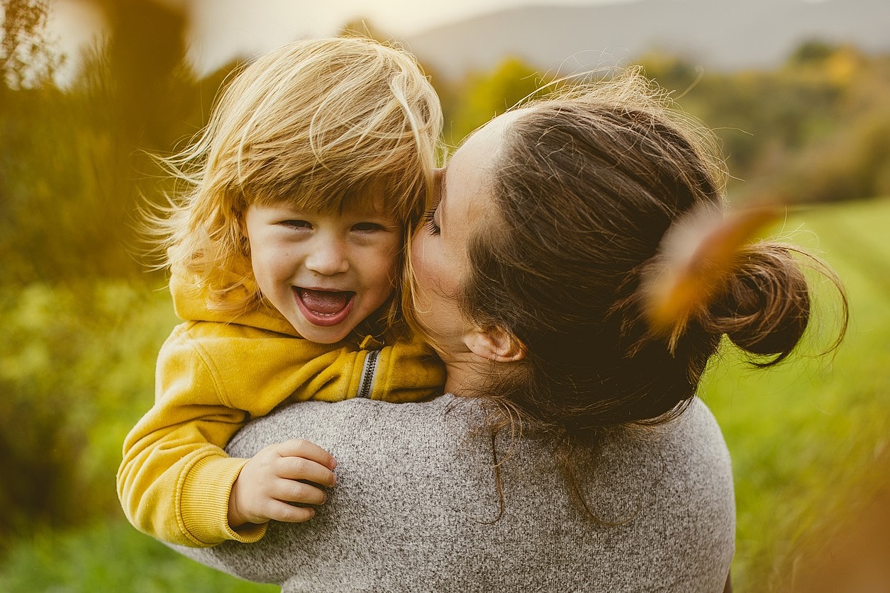 Eine junge Frau steht mit dem Rücken zu Kamera und hat ihre Tochter im Arm.
