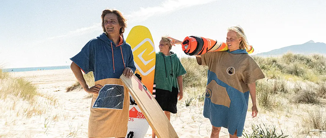 Gruppe von jungen Leuten am Strand mit Surfponchos von Wave Hawaii