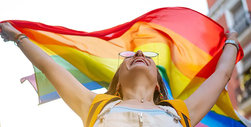 Eine junge Frau hält eine Regenbogenflagge über ihren Kopf.