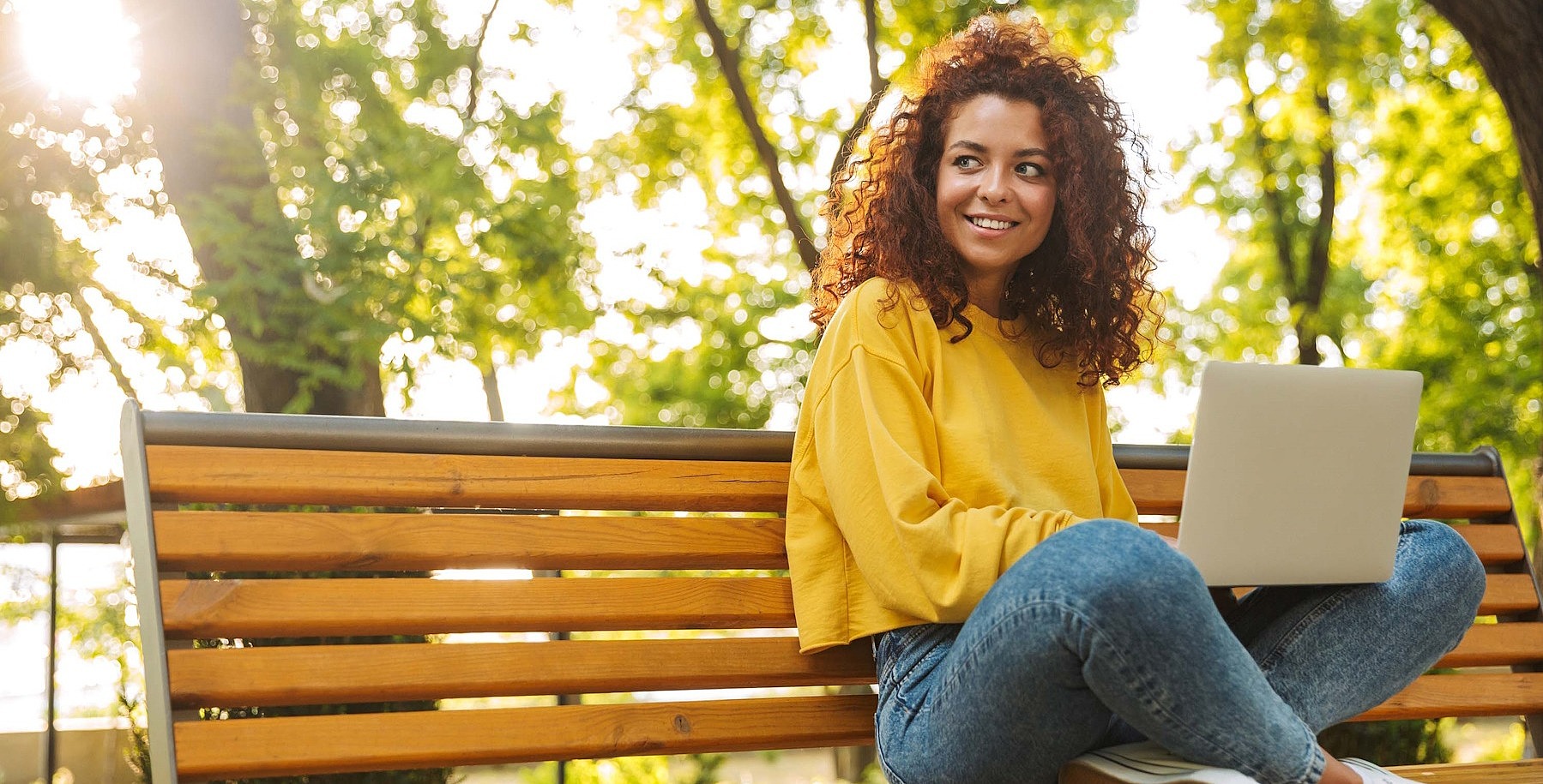 Junge Frau sitzt mit einem Laptop auf einer Parkbank