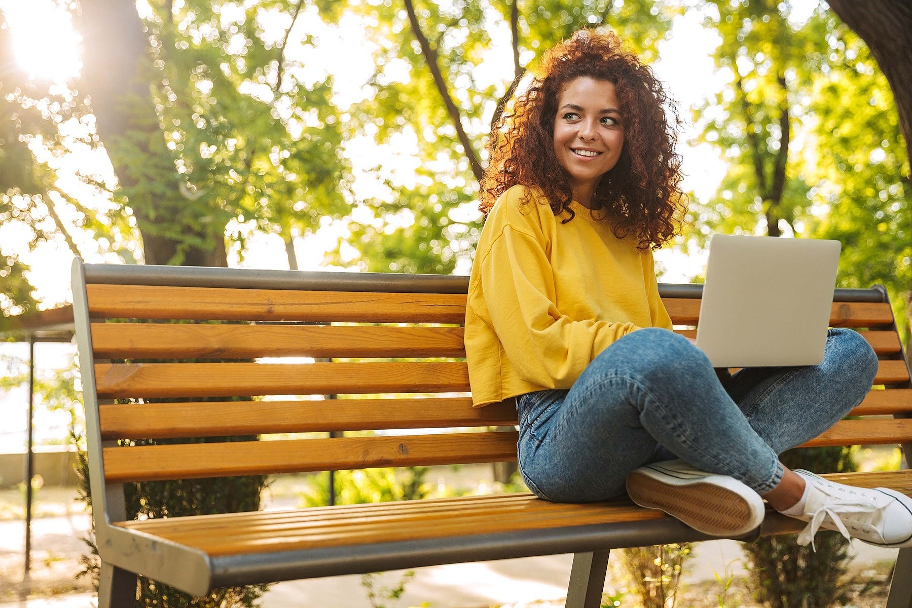 Junge Frau sitzt mit einem Laptop auf einer Parkbank