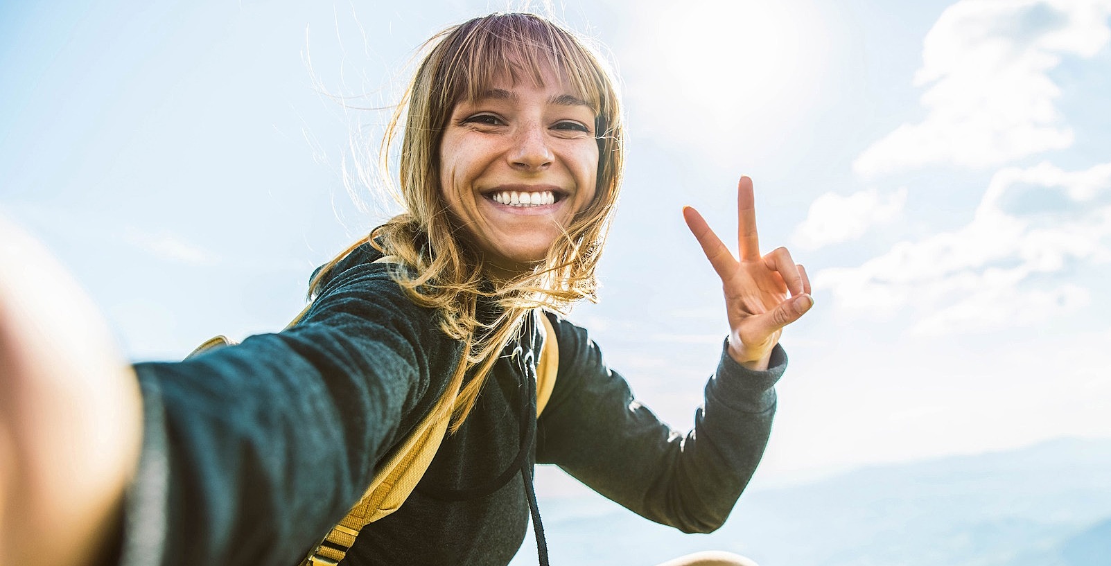 Junge Frau auf einer Bergwiese macht ein Peace-Zeichen