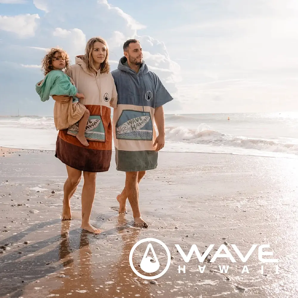 Eltern mit Kleinkind auf dem Arm am Strand mit Wave Hawaii Ponchos