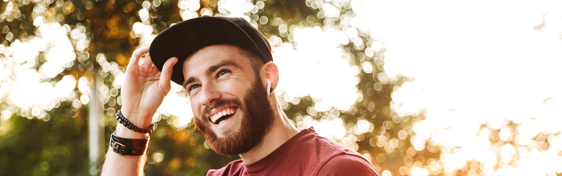 Ein junger Mann schaut lächelnd an der Kamera vorbei und greift sich an den Schirm seiner Cap.