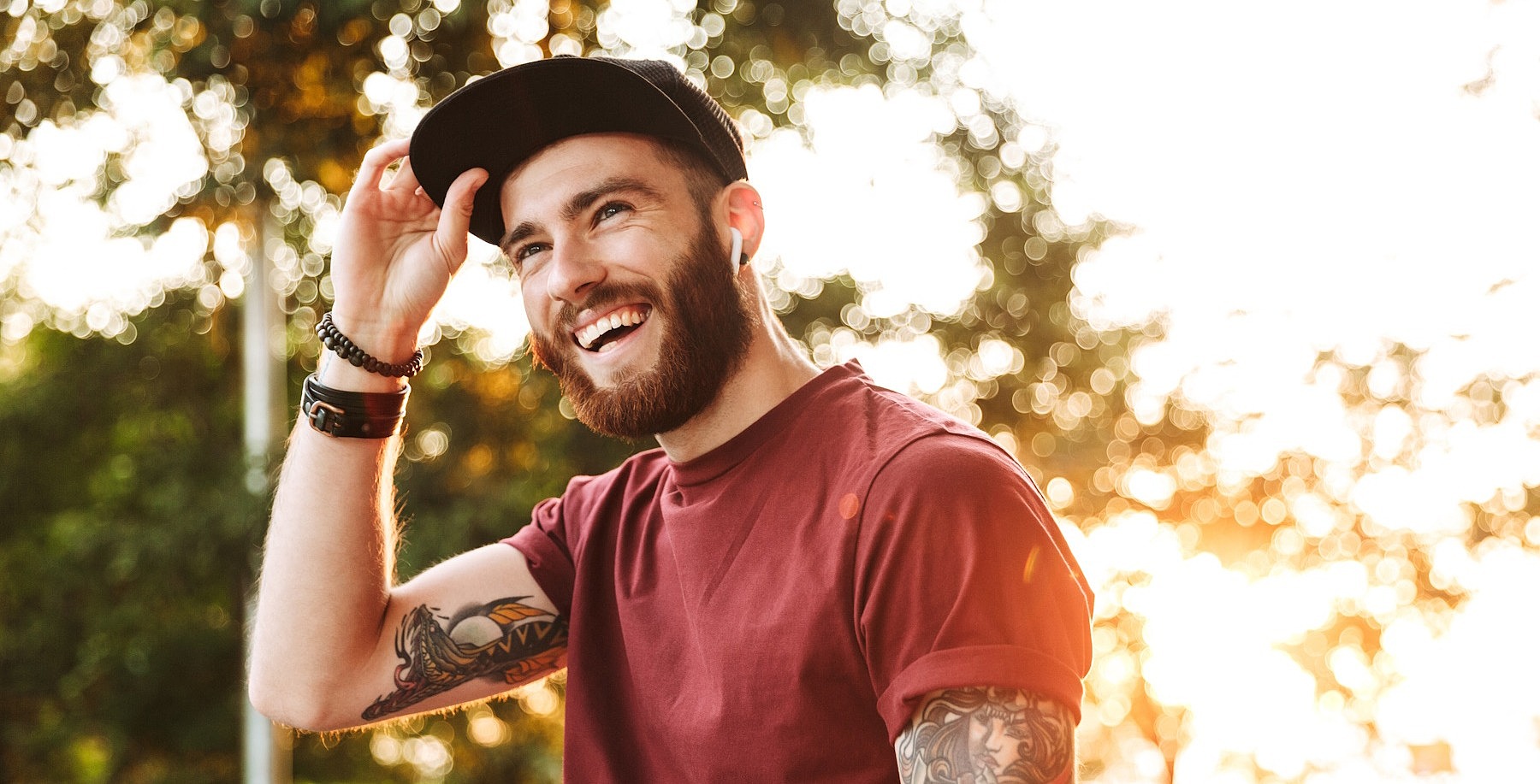 Ein junger Mann schaut lächelnd an der Kamera vorbei und greift sich an den Schirm seiner Cap.