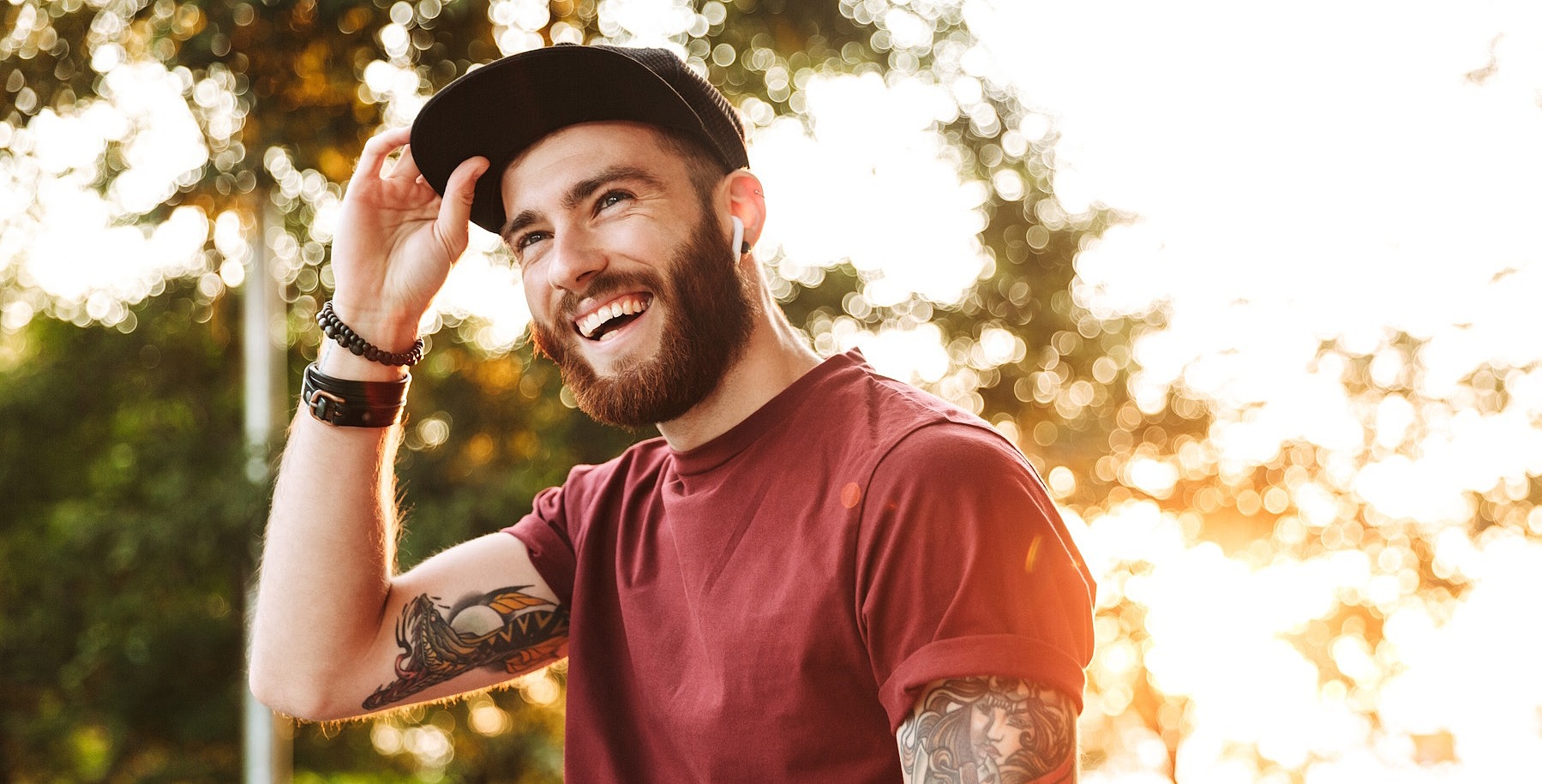 Ein junger Mann schaut lächelnd an der Kamera vorbei und greift sich an den Schirm seiner Cap.