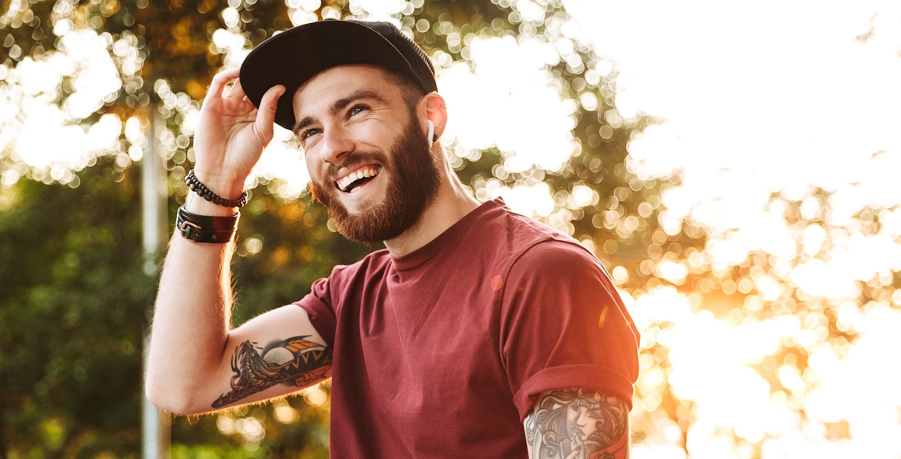 Ein junger Mann schaut lächelnd an der Kamera vorbei und greift sich an den Schirm seiner Cap.