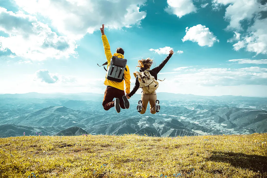 Ein Paar springt vor einer Bergkulisse vor Freude in die Luft