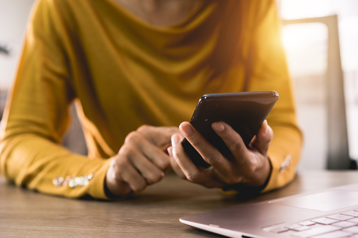 Eine Frau mit einem gelben Oberteil tippt auf ihrem Smartphone.