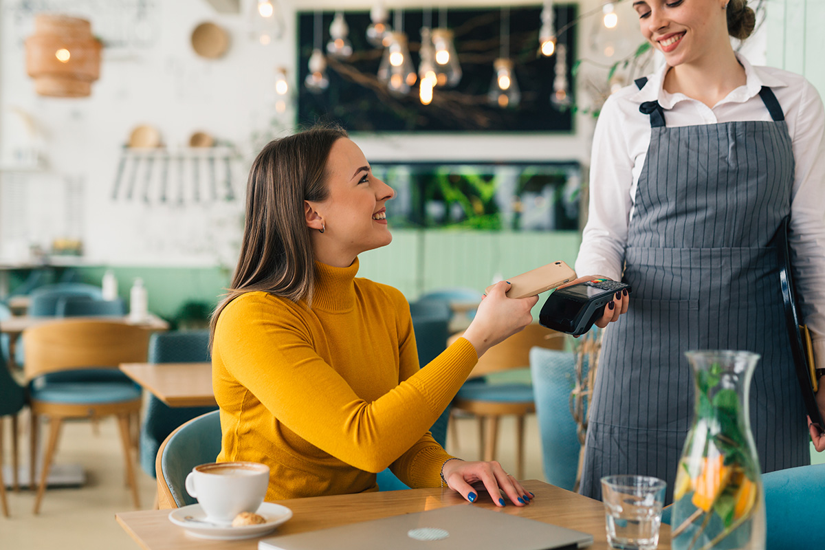 Eine Frau bezahlt in einem Café ihren Kaffee bei der Kellnerin mit Karte.