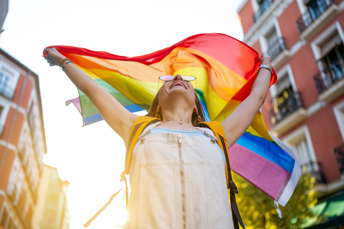 Eine junge Frau hält eine Regenbogenflagge über ihren Kopf.